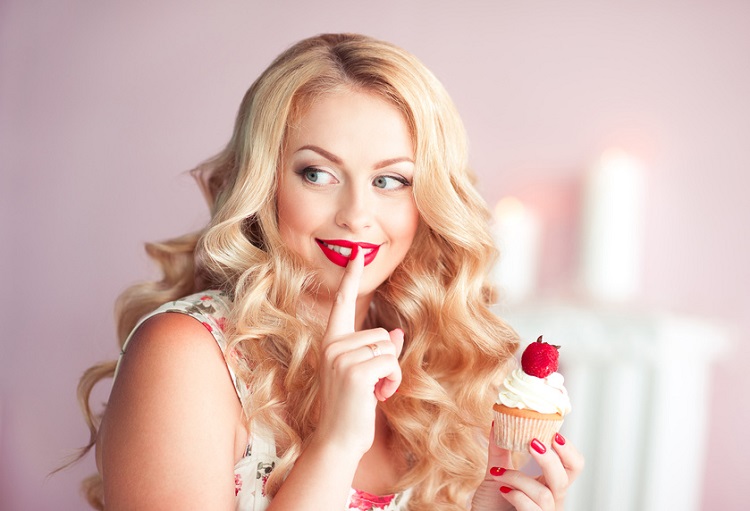 Smiling woman holding cupcake with strawberry in room. Looking away.