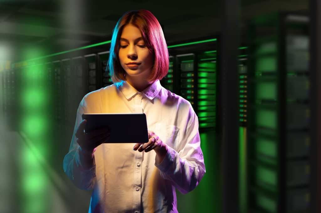 Hosting provider employee. Woman in data center. Girl with tablet computer. Woman indoors hosting company. Career in hosting business. Woman manager near green server rack. Telecommunication business